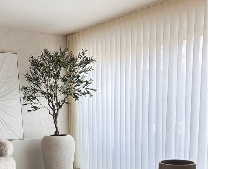 Halfdoorschijnende gordijnen in wavevouwen langs een hele raamwand, met een olijfboom ervoor