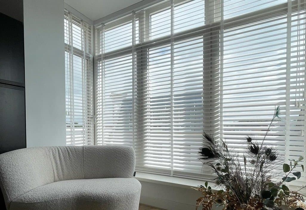 Hoekraam met witte houten jaloezieën die strepen zonlicht op de vloer werpen