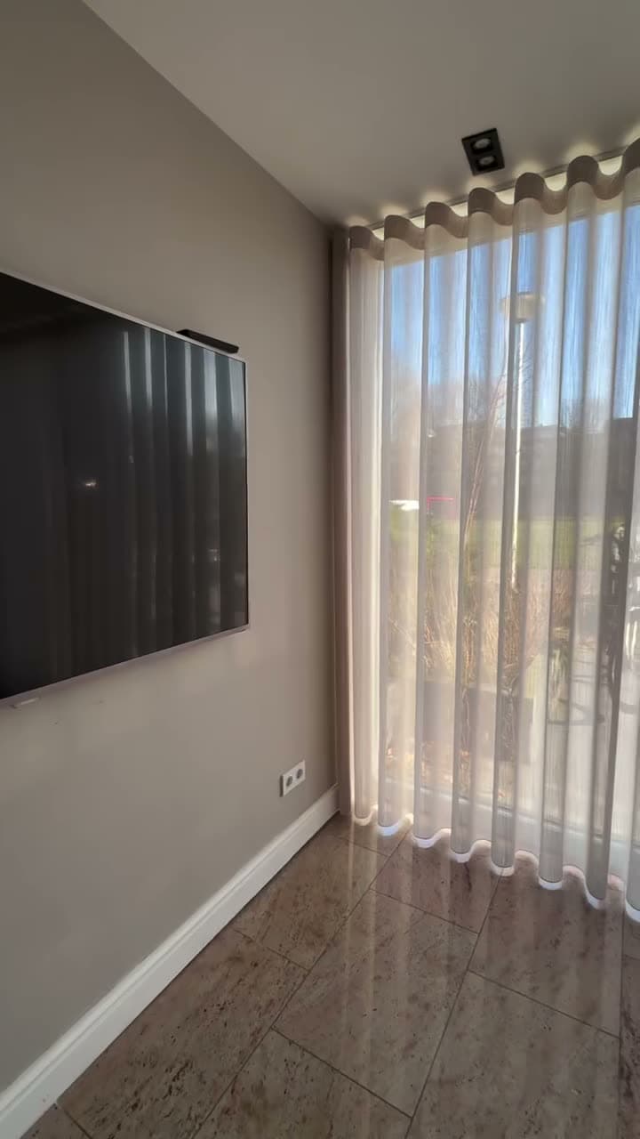 Woonkamer met een wand witte vitrage in wavevouwen, met zonlicht dat erdoorheen valt
