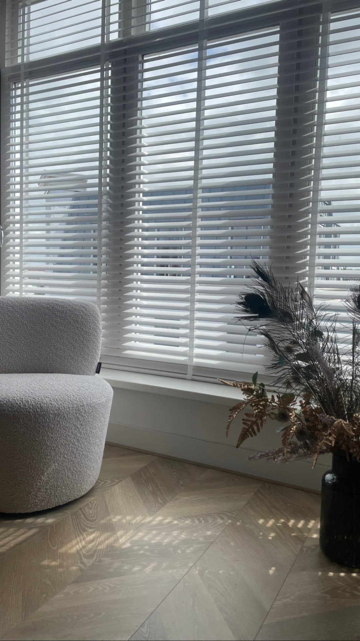 Woonhoek met witte houten jaloezieën; gestippeld licht op de visgraatvloer