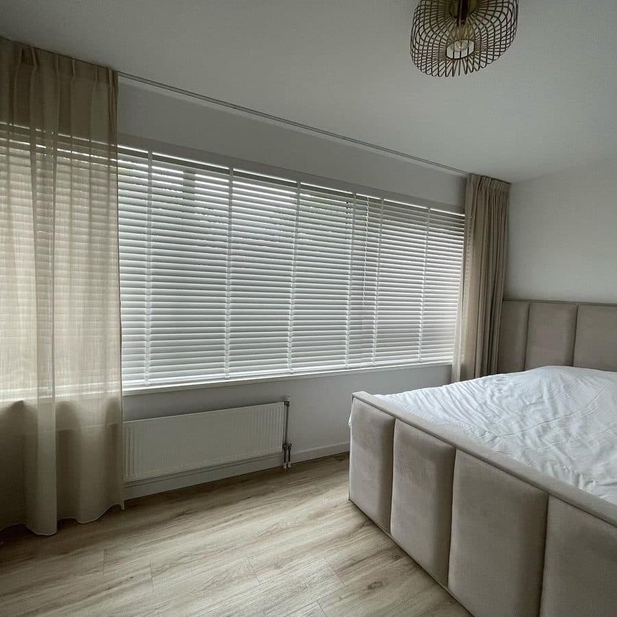 Slaapkamer met witte jaloezie over een breed raam