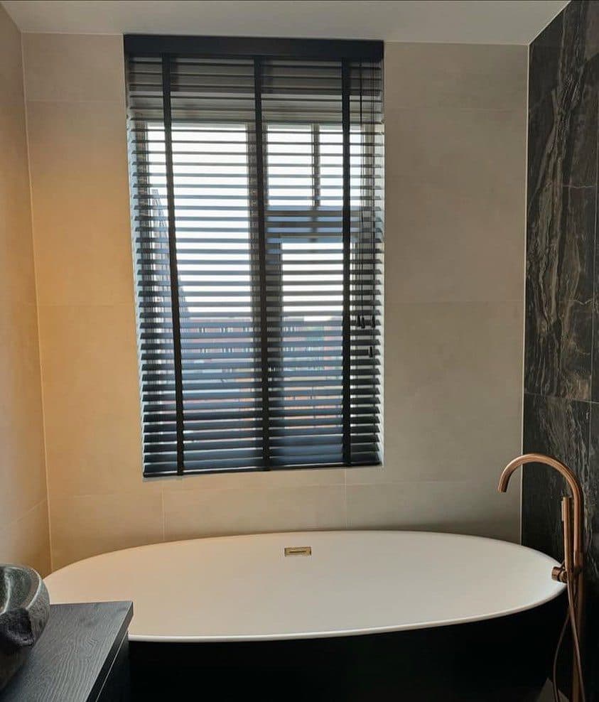 Badkamer met vrijstaand bad en een zwarte jaloezie voor het raam