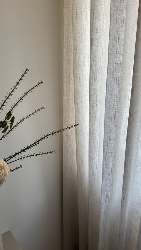 Detail van een linnen inbetween in rustige plooien tegen een lichte wand, met een droge tak ervoor